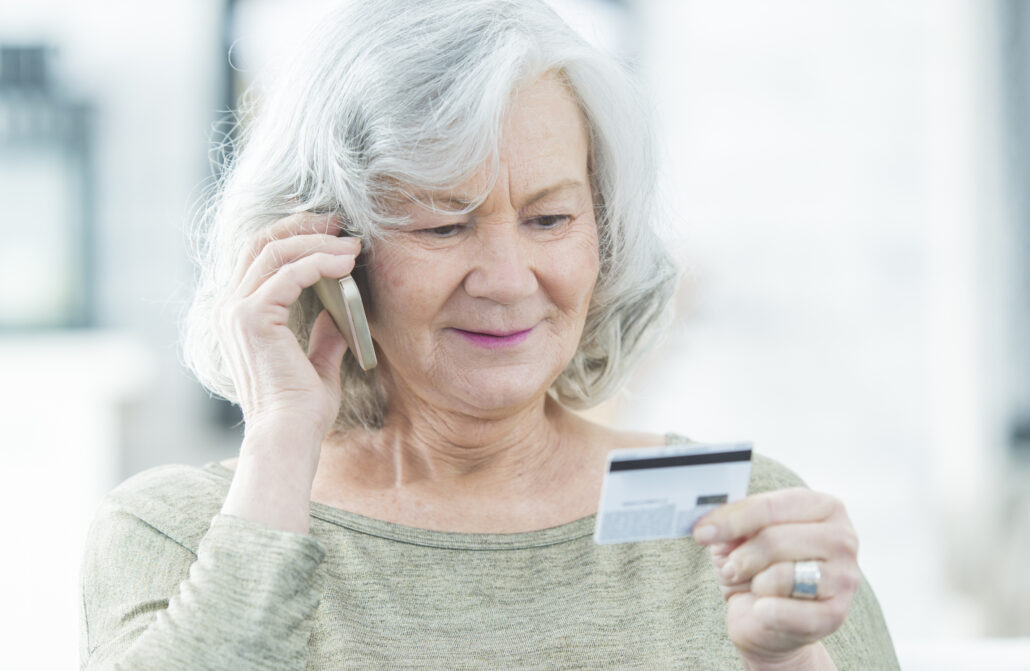 Ältere Frau am Telefon mit Kreditkarte in der Hand